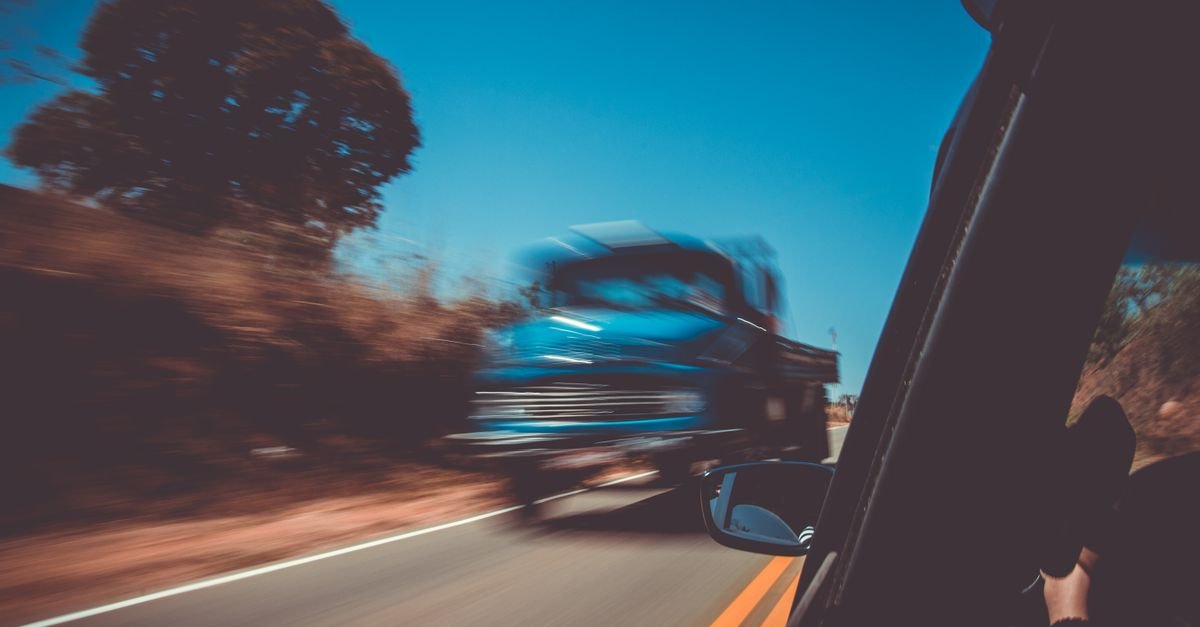 Caminhão azul em movimento em rodovia de pista simples com faixa central amarela