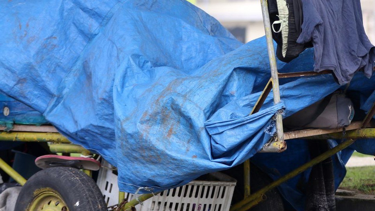 Carrinho com pertences cobertos por lona azul em calçada
