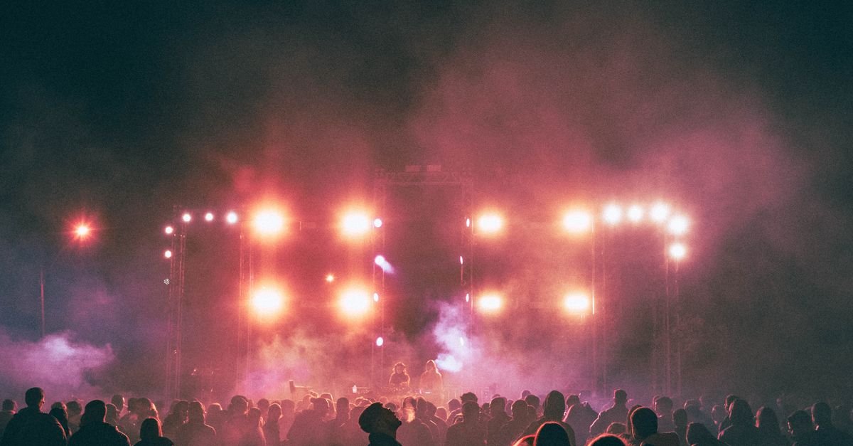 Público em silhueta diante de palco iluminado ao ar livre durante festival de música à noite