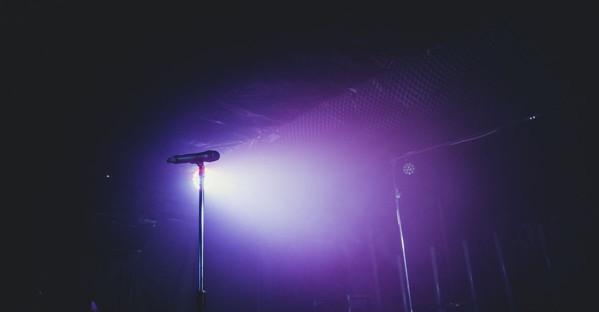 Microfone em pedestal sobre palco iluminado por luz roxa