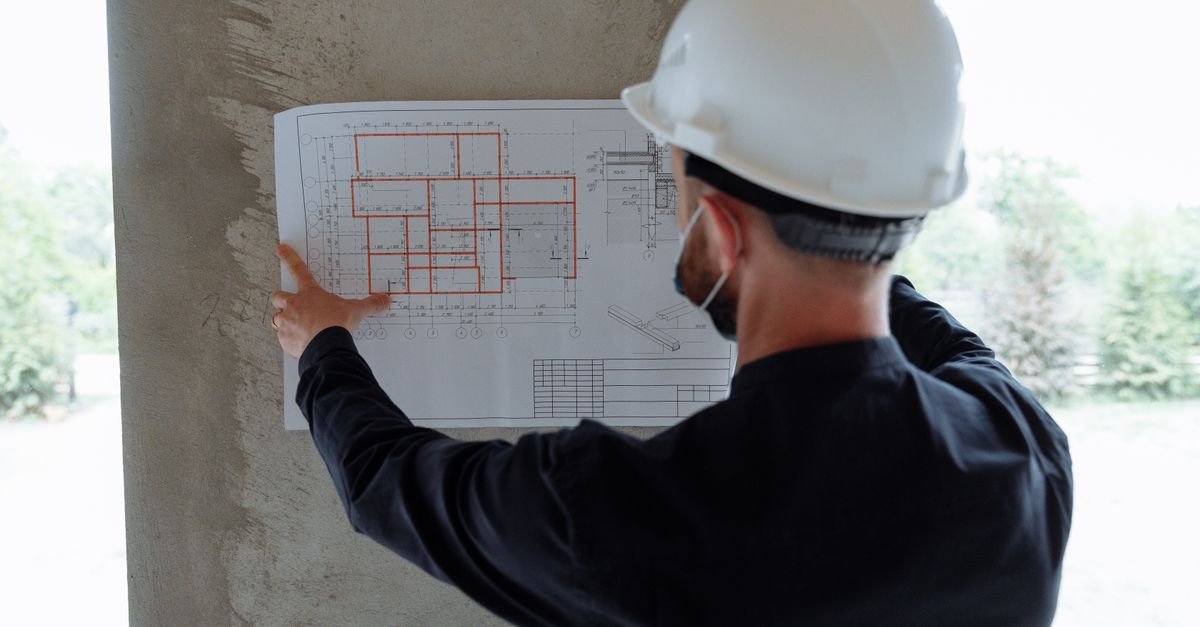 Trabalhador de capacete branco analisando planta em canteiro de obras