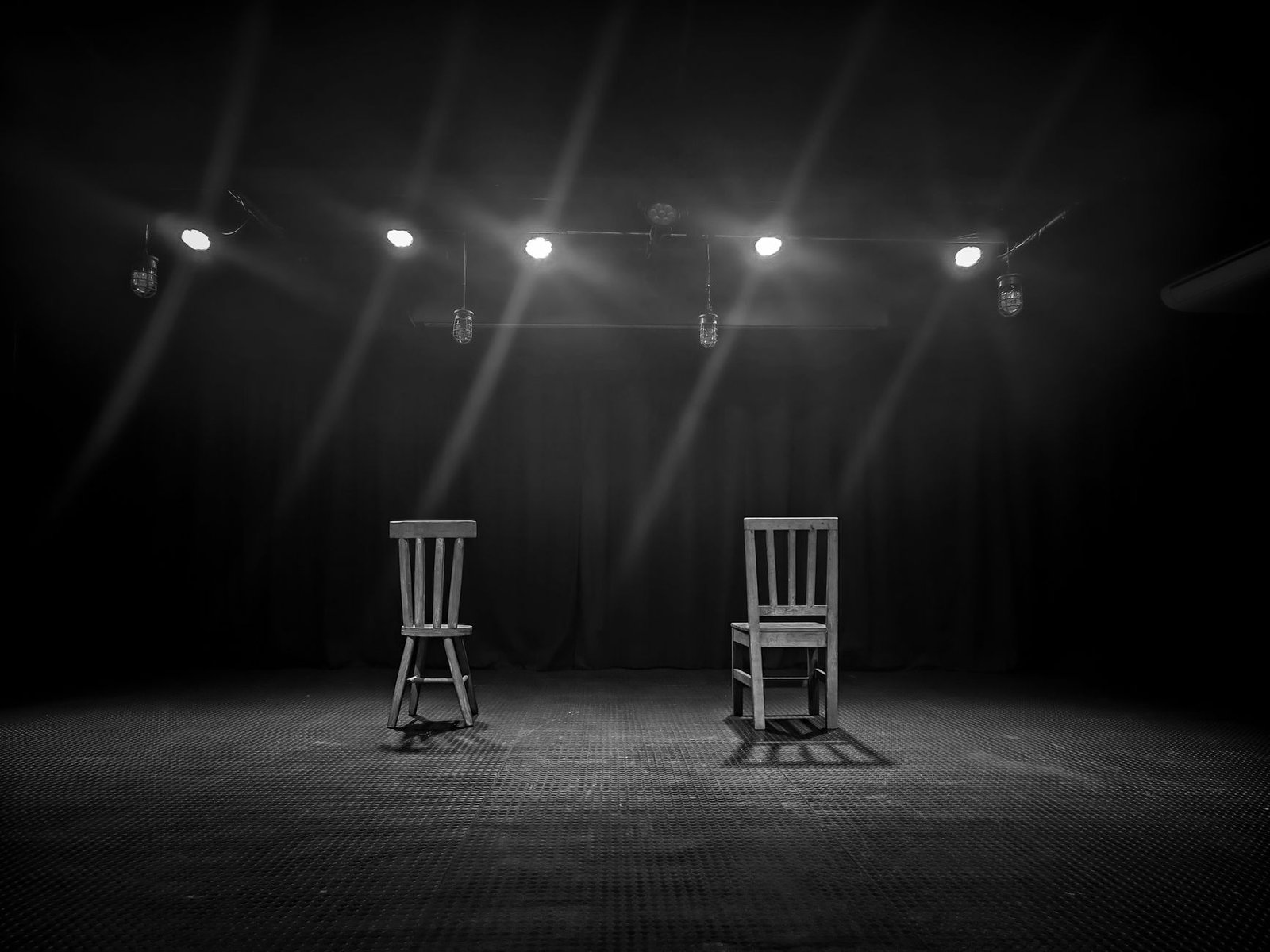 Palco escuro com duas cadeiras de madeira sob holofotes