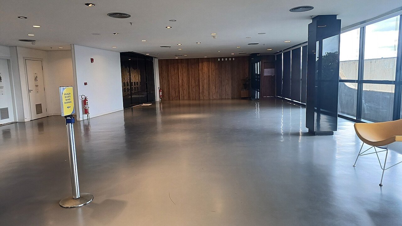 Saguão de circulação do CCBB Brasília, com piso cinza, painel de madeira ao fundo e totem de sinalização da Coleção de Arte Banco do Brasil
