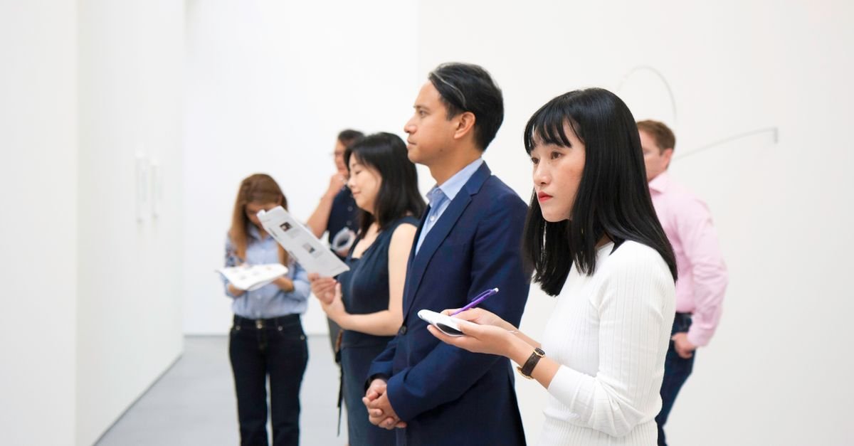 Grupo de visitantes observa obras em uma galeria de arte de paredes brancas