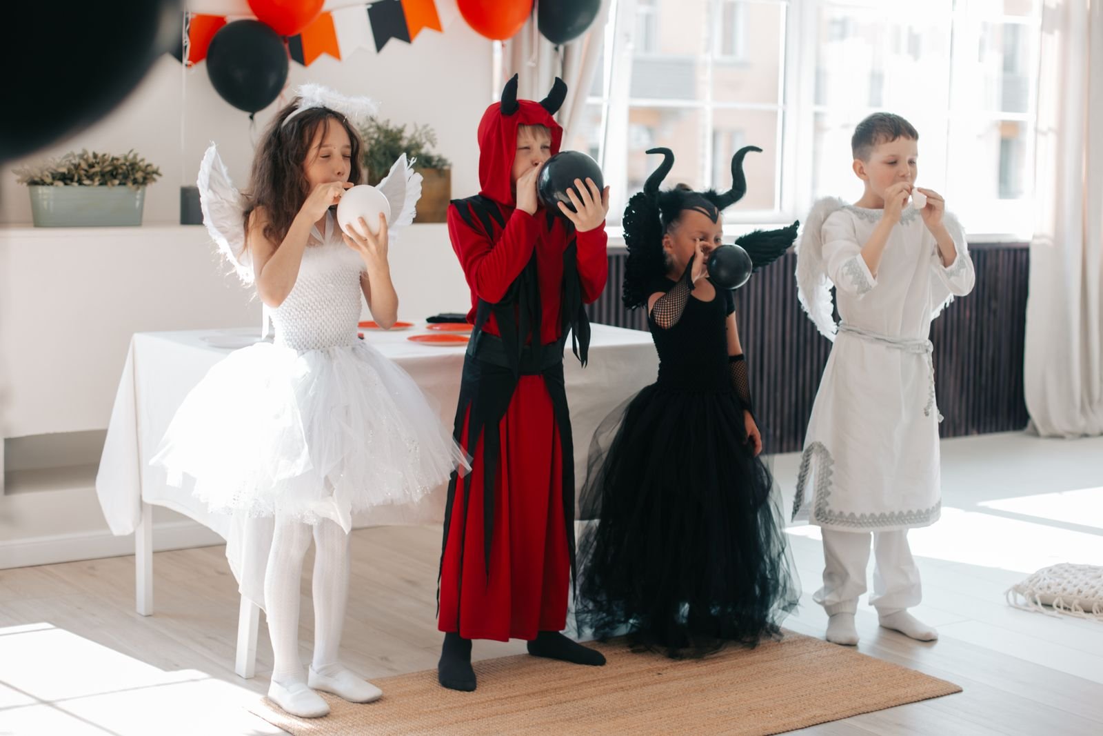 Quatro crianças fantasiadas de anjo e diabo enchem balões em uma sala decorada para o Halloween (foto ilustrativa)