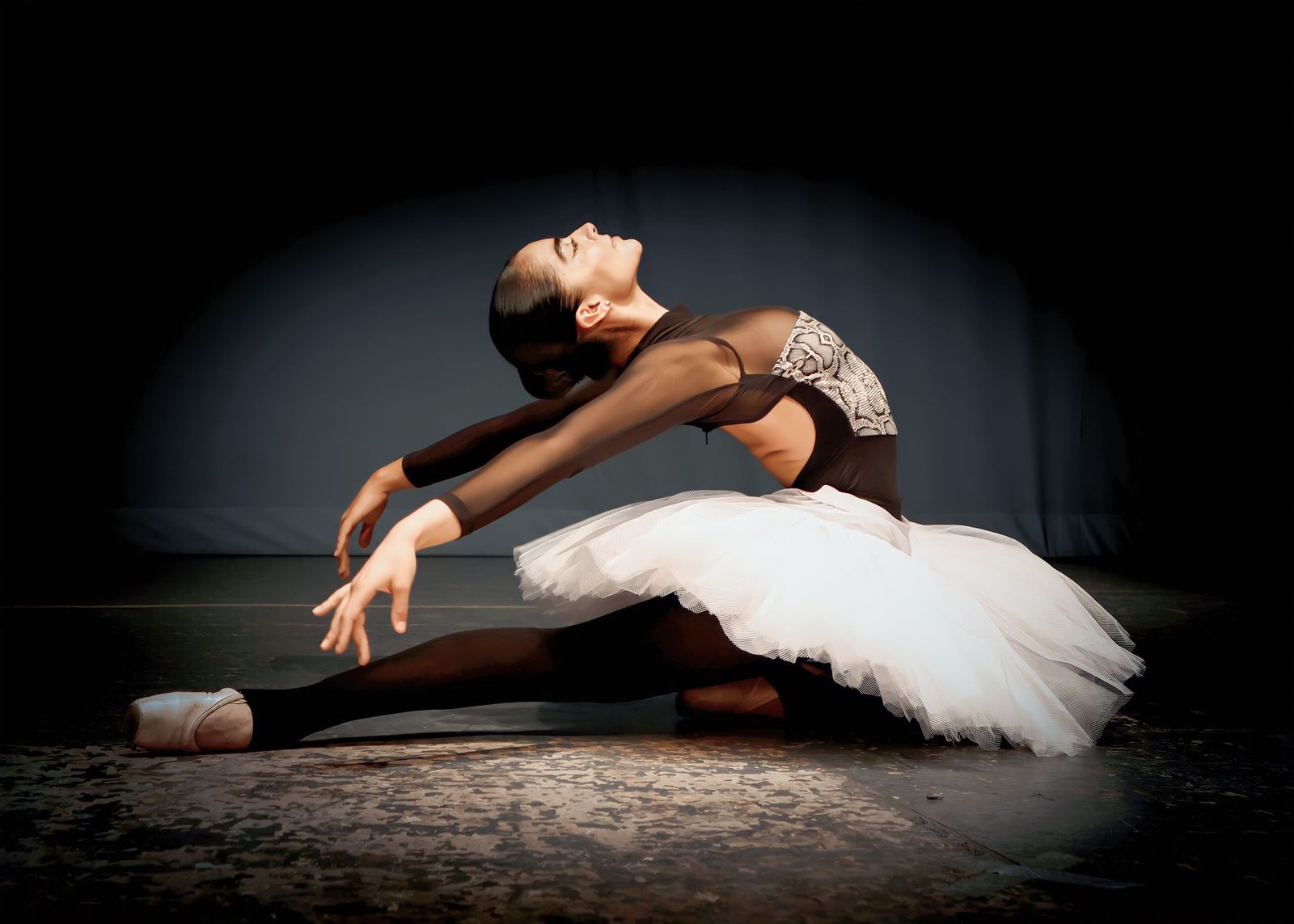 Bailarina de tutu branco em pose de balé sob um foco de luz em palco escuro