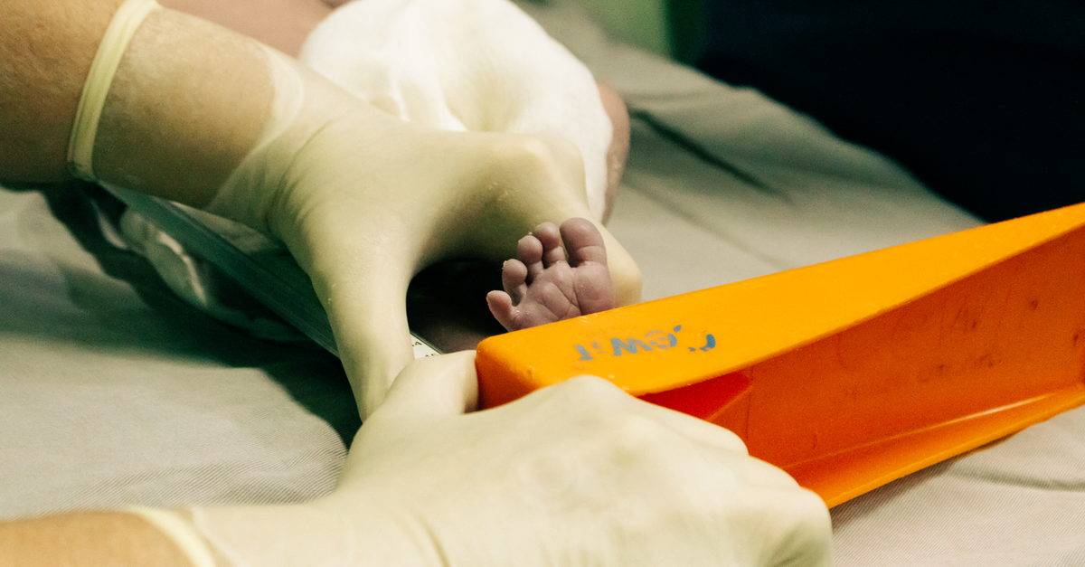 Profissional de saúde com luvas mede o pé de um recém-nascido em maternidade