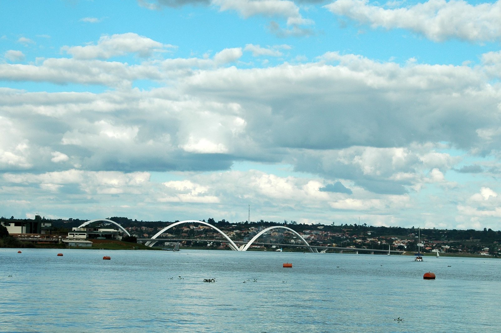 Arcos da Ponte JK vistos da água do Lago Paranoá, com veleiros ao fundo