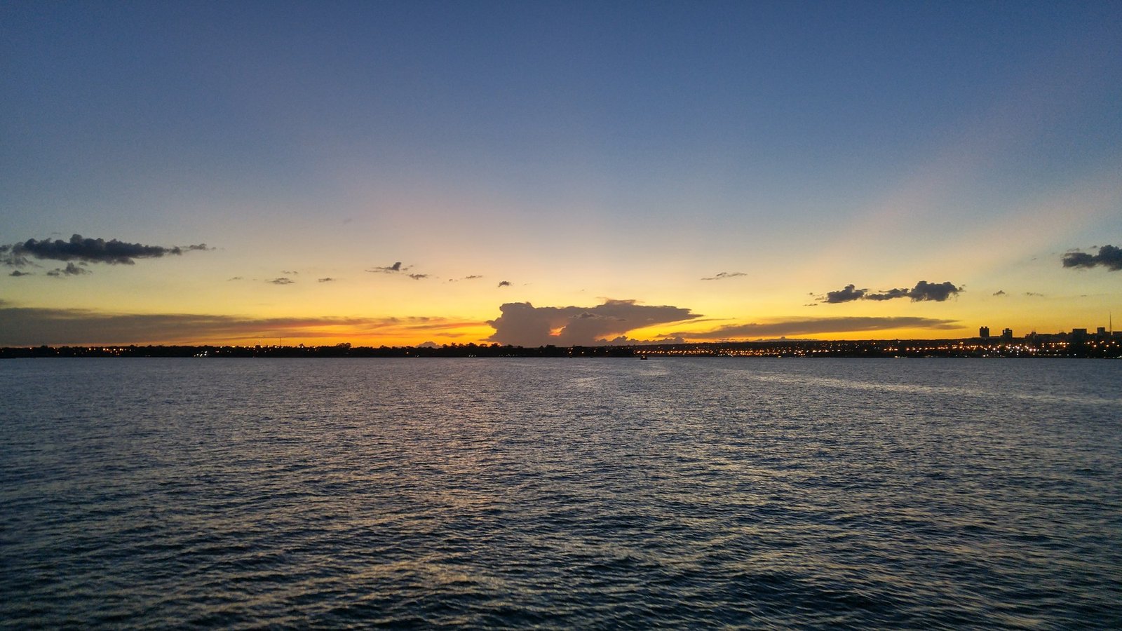 Lago Paranoá ao entardecer, com o céu alaranjado e as luzes da orla ao fundo