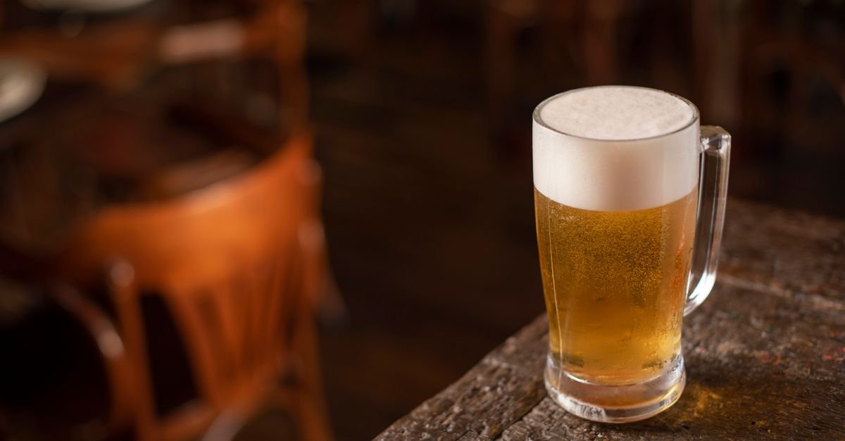 Caneca de chope com colarinho sobre mesa de madeira em ambiente de bar