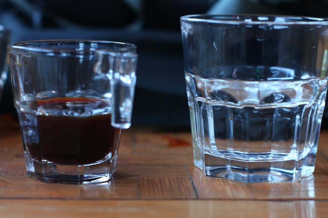Copo com café coado ao lado de copo de água sobre mesa de madeira