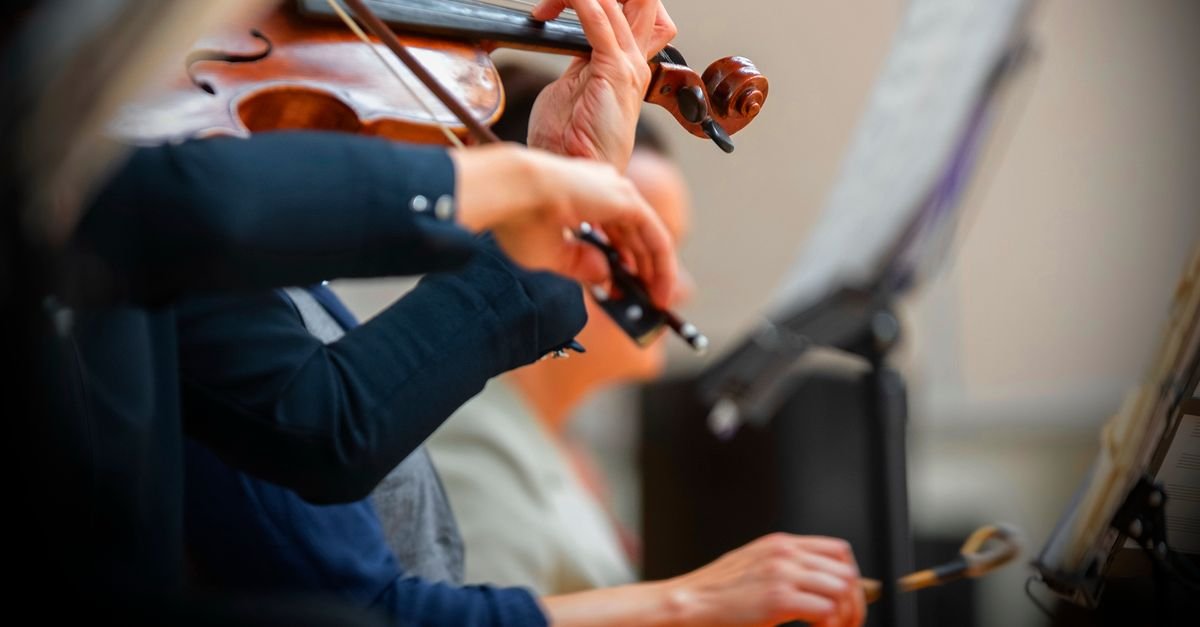Violinistas tocam durante apresentação de orquestra, em plano fechado nos instrumentos