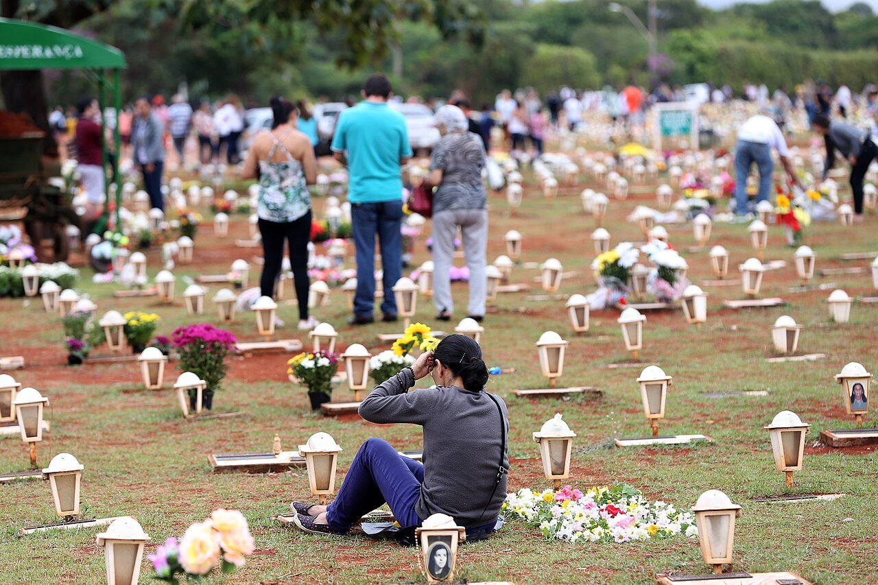 Visitantes caminham entre sepulturas rasas com lanternas e flores no cemitério Campo da Esperança, em Brasília, durante o Dia de Finados