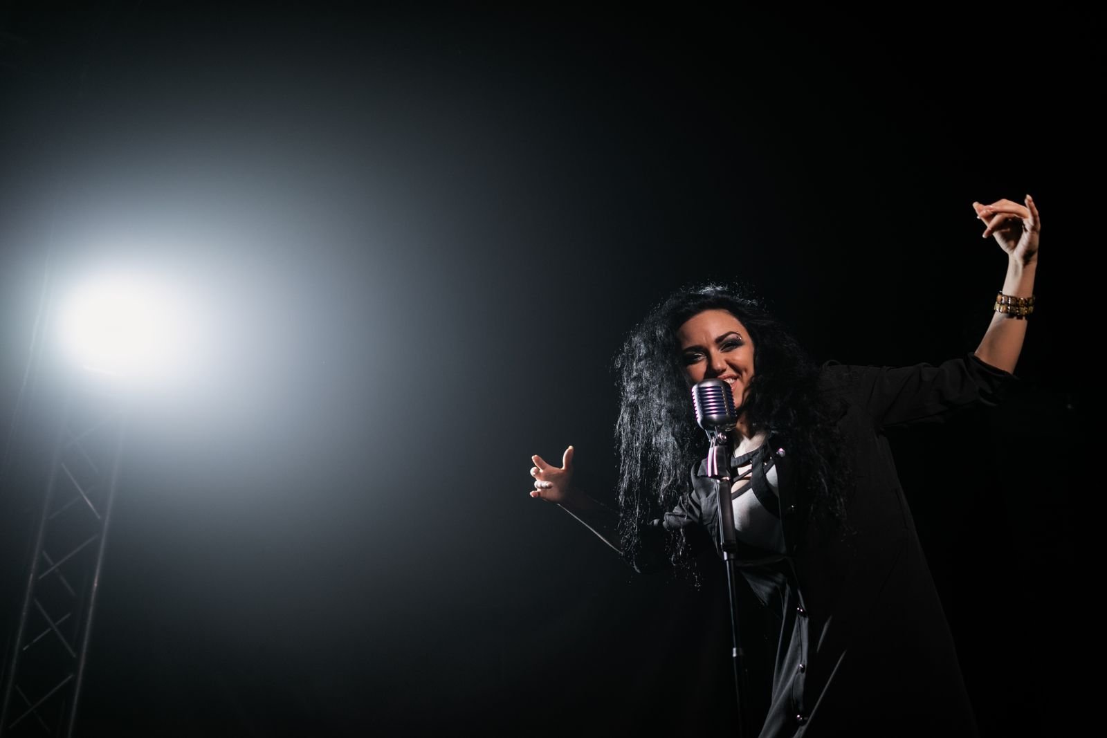 Cantora em palco escuro diante de microfone vintage, iluminada por um holofote lateral