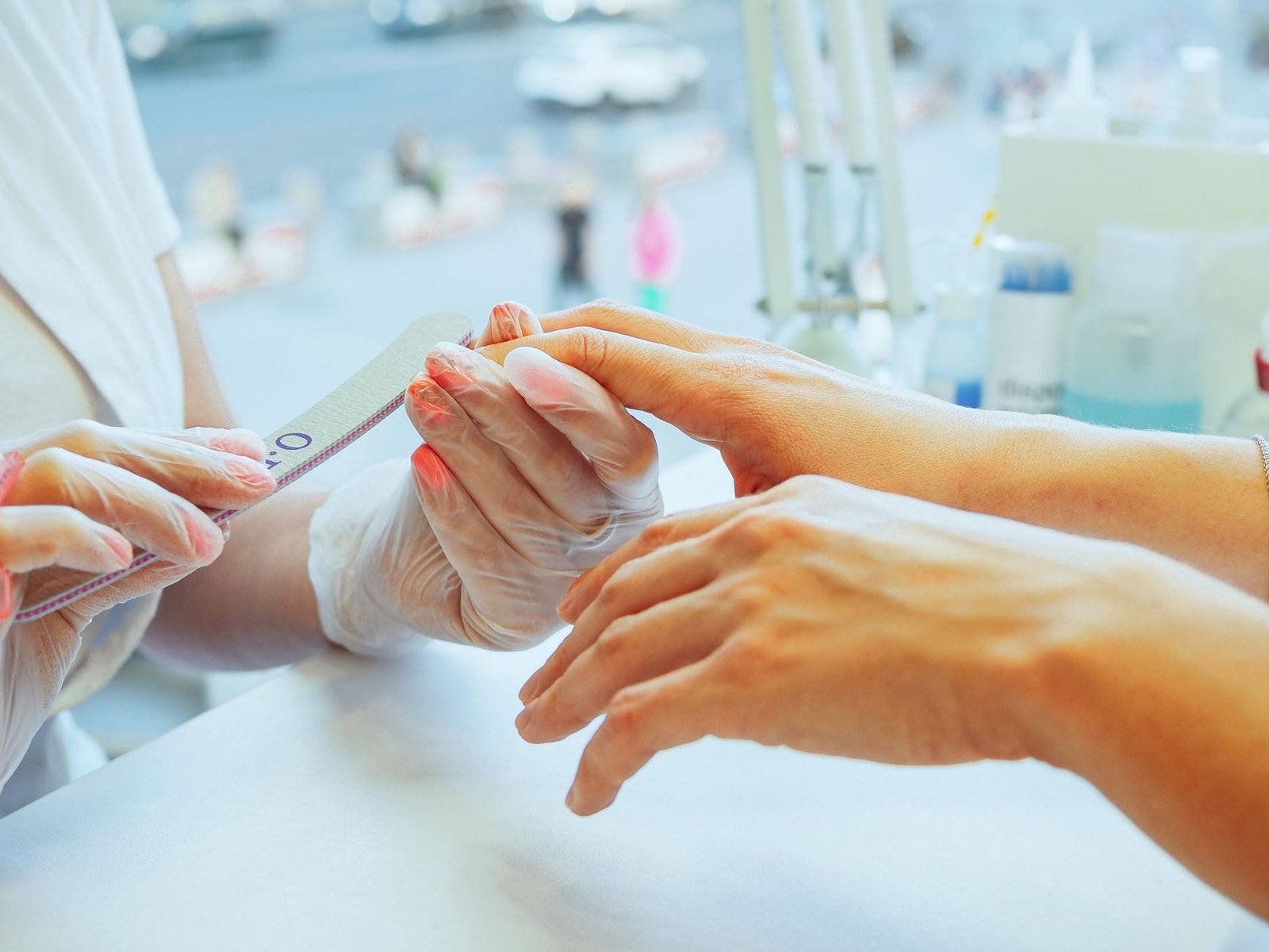 Close de mãos durante aula de manicure, com lixa e luvas descartáveis