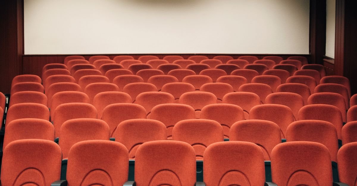 Fileiras de poltronas vermelhas vazias diante da tela de uma sala de cinema