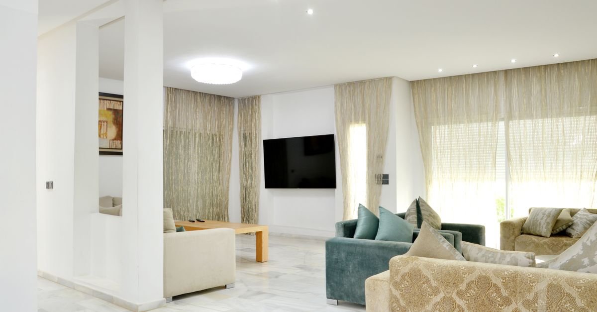 Sala de estar ampla com sofás claros, poltronas e cortinas até o teto