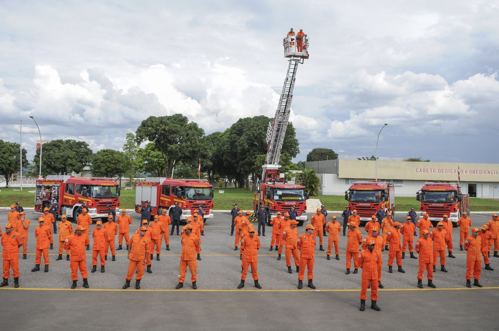 Militares do Corpo de Bombeiros em formatura, com viaturas vermelhas ao fundo