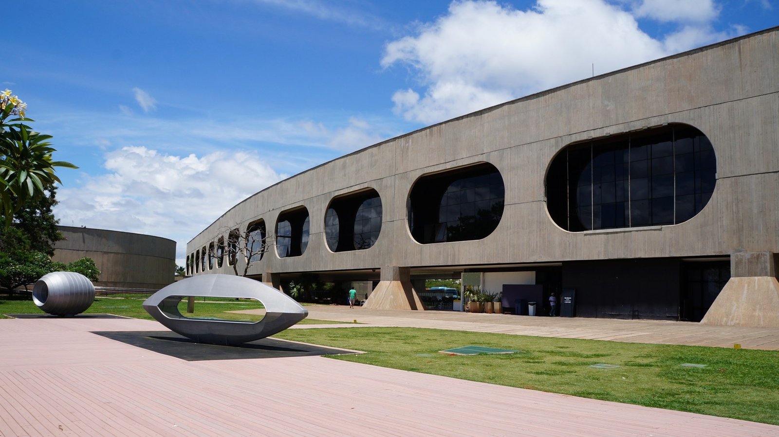 Fachada curva de concreto com janelas ovais do CCBB Brasília e esculturas metálicas no jardim, em foto de arquivo