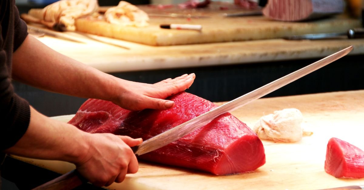 Chef corta um lombo de atum fresco com faca longa sobre tábua de madeira
