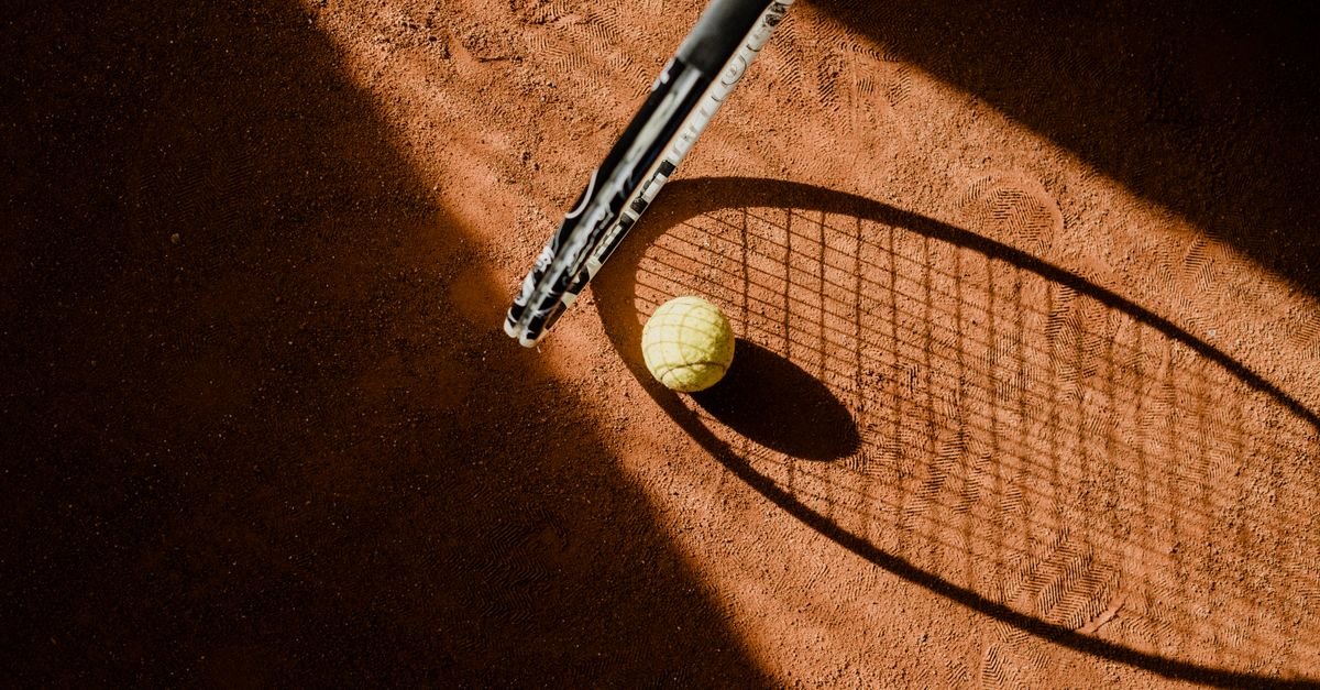 Bola de tênis e sombra de raquete sobre quadra de saibro