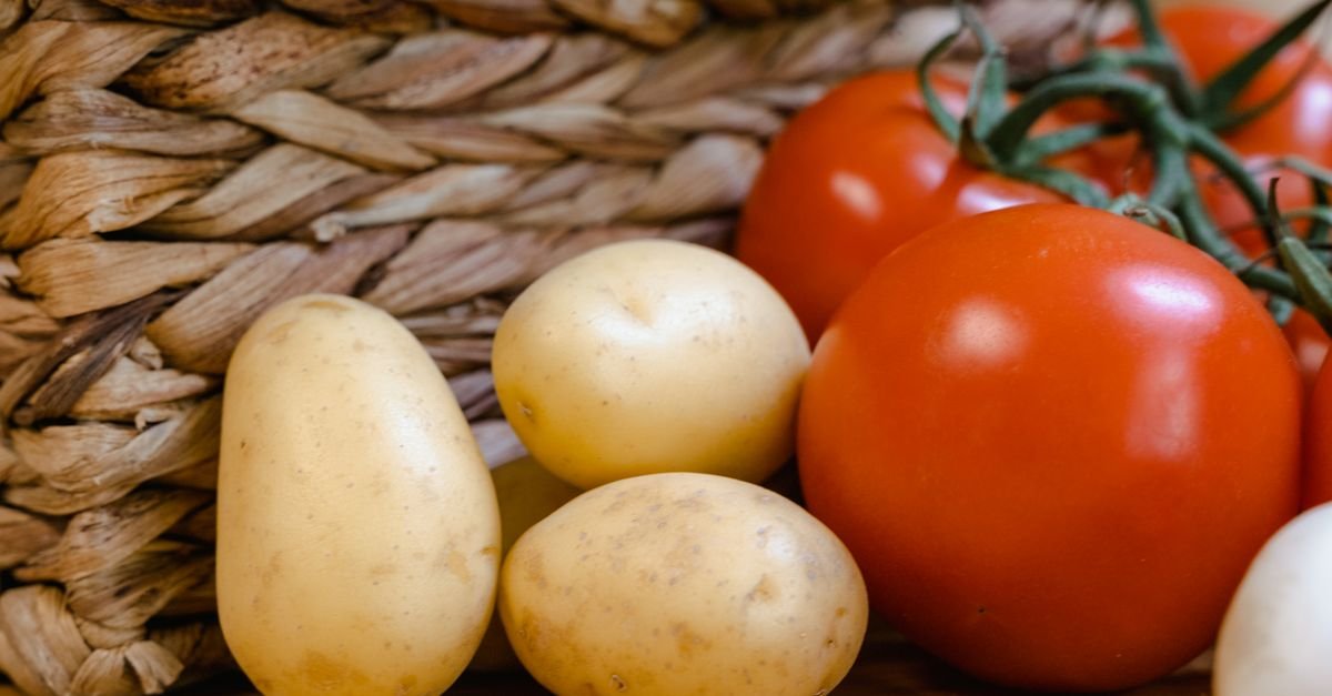 Batatas e tomates maduros em closeup ao lado de cesta de palha
