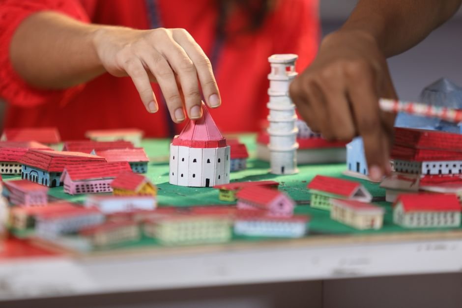 Mãos montando casas de papel coloridas em uma maquete de cidade