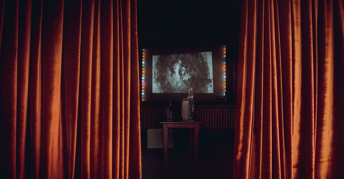 Sala de cinema com cortinas abertas e filme projetado na tela