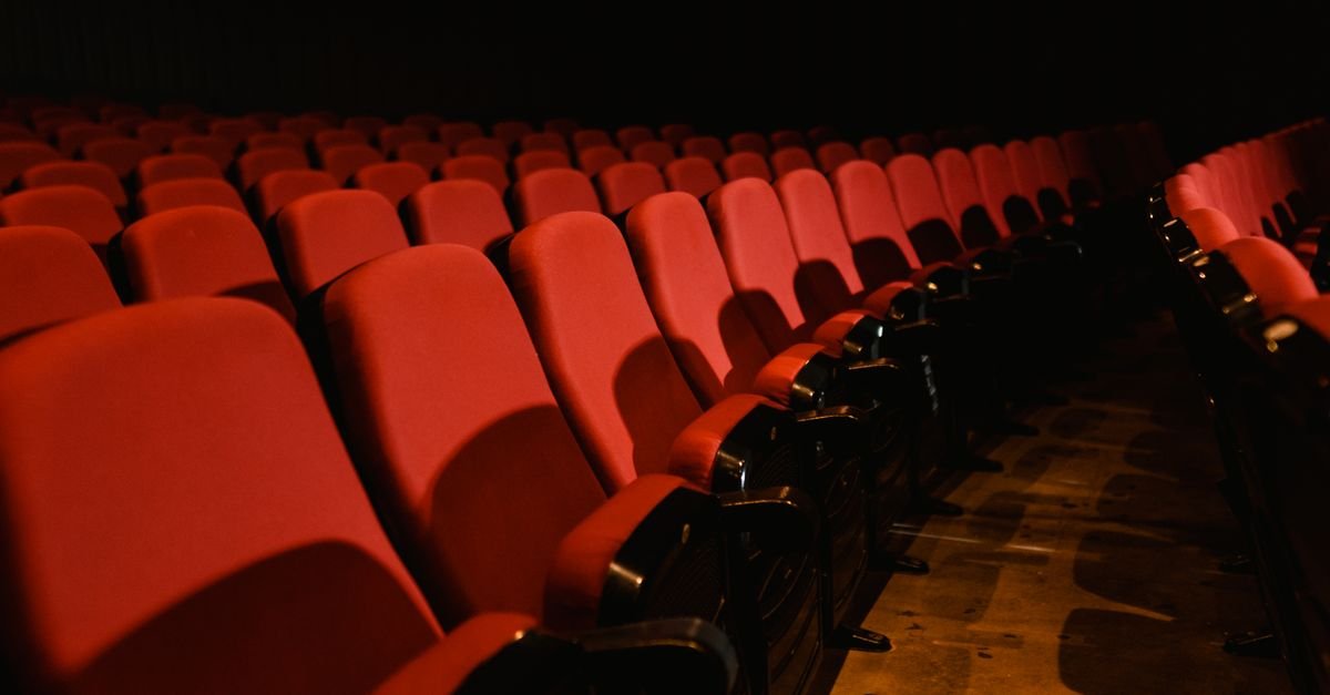Fileiras de poltronas vermelhas vazias em sala de cinema com luz baixa