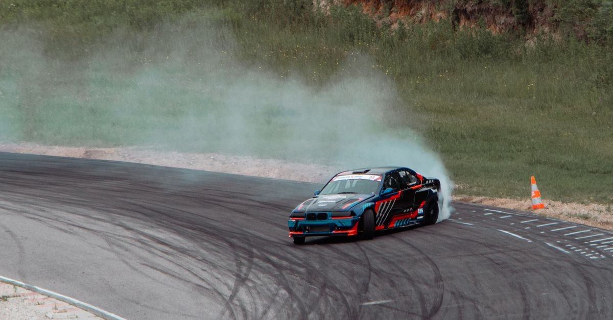 Carro esportivo derrapando em curva de autódromo com fumaça saindo dos pneus