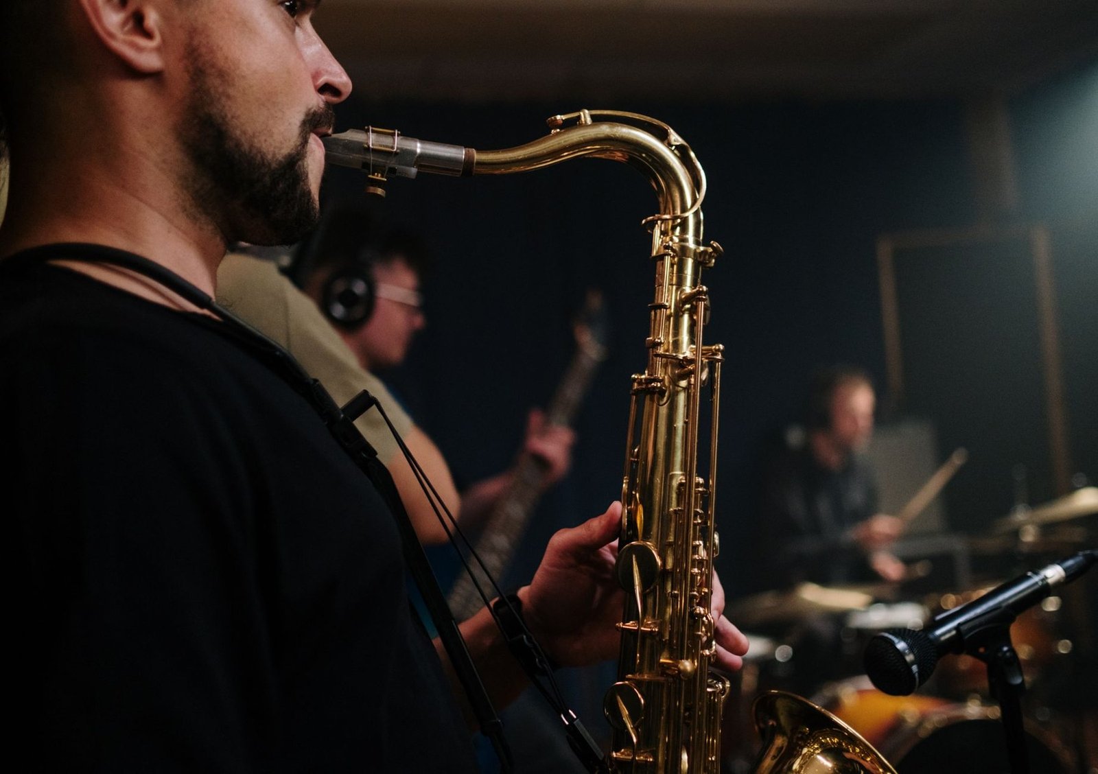 Saxofonista toca ao lado de contrabaixista e baterista em palco escuro