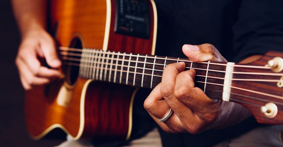 Mãos de músico tocando violão de aço em close