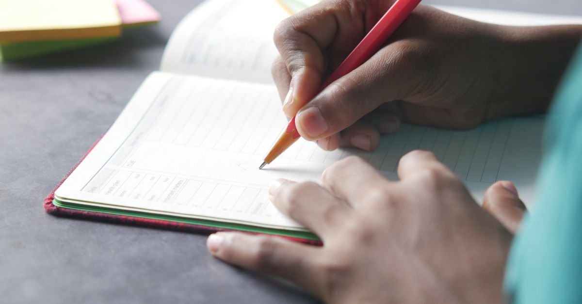 Mão escrevendo com caneta em caderno aberto sobre mesa escura