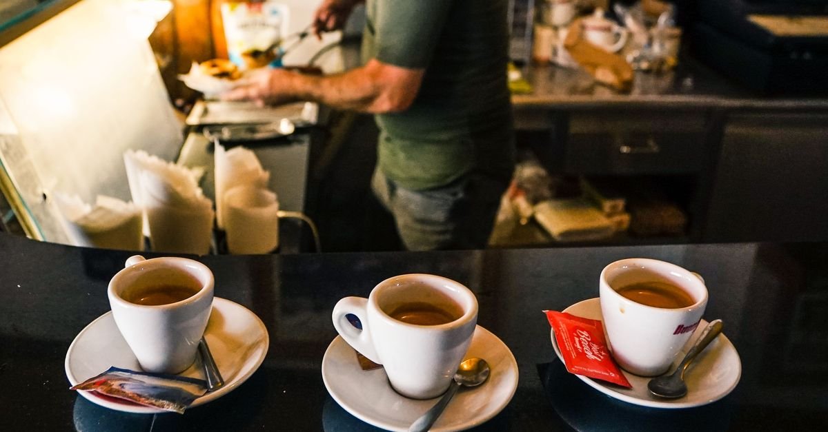 Três xícaras de café espresso sobre balcão de cafeteria com barista ao fundo