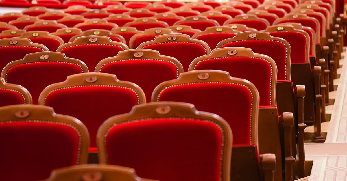 Fileiras de poltronas de veludo vermelho numeradas na plateia vazia de um teatro