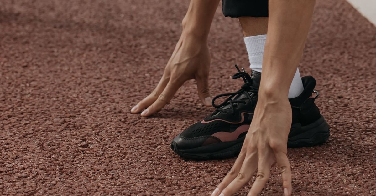 Mãos e tênis de corredor posicionados na linha de largada de uma pista de atletismo