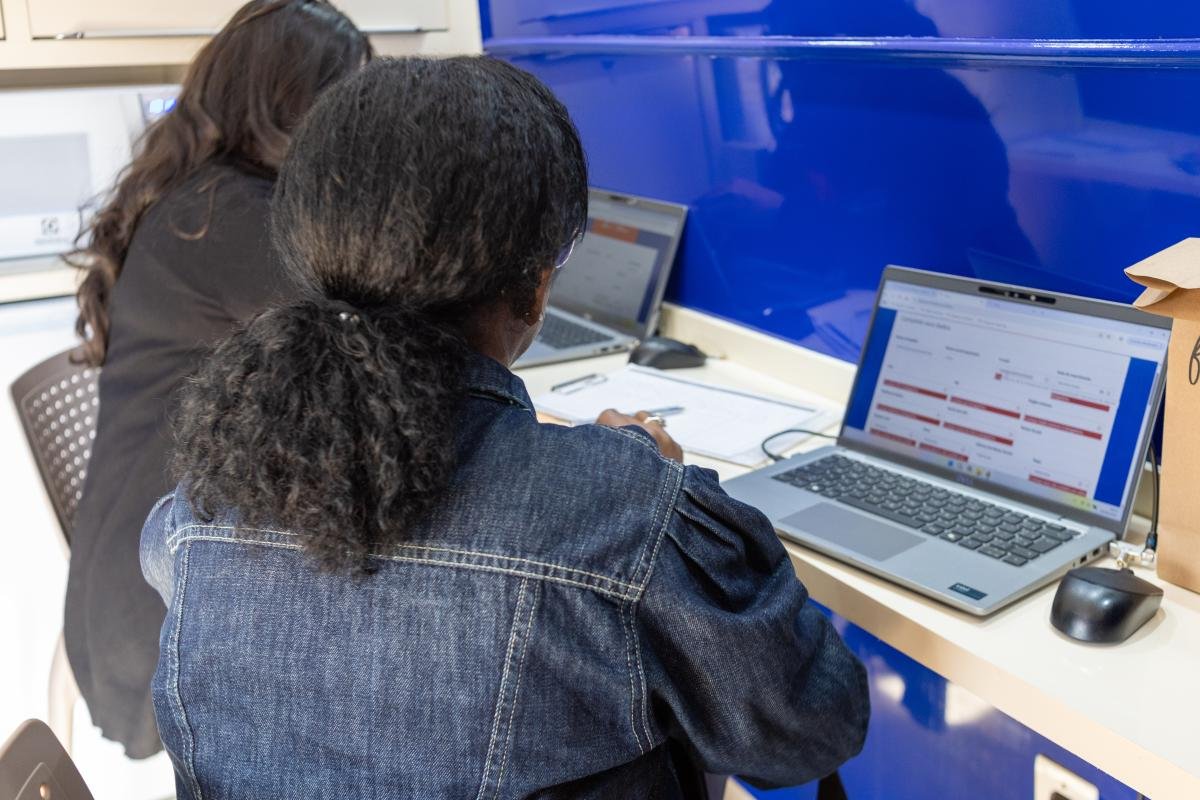 Duas mulheres de costas preenchem formulário em notebook durante atendimento