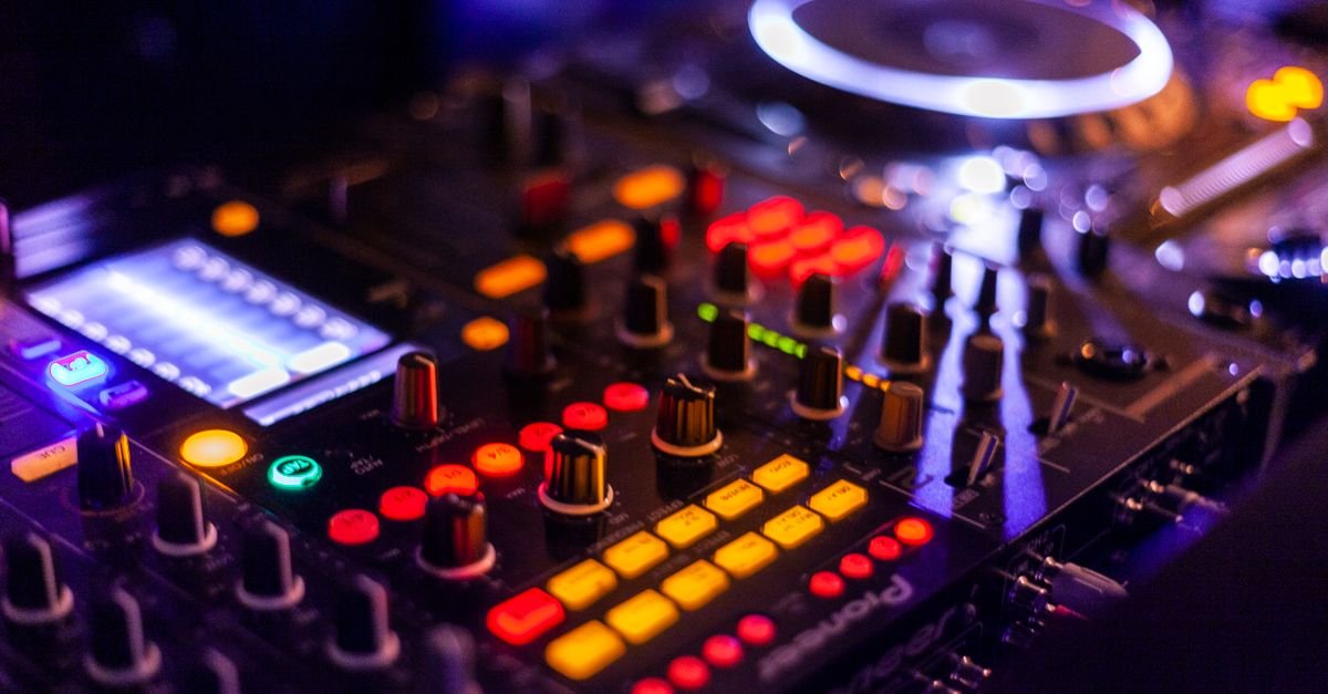 Mesa de mixagem de DJ iluminada por luzes coloridas durante festa