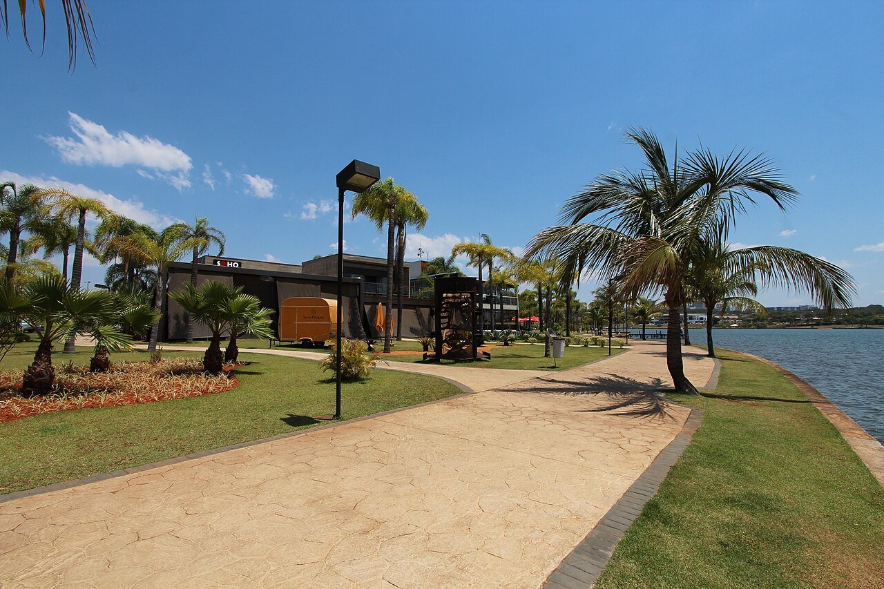 Calçada ao lado do Lago Paranoá no Pontão do Lago Sul, com palmeiras e restaurantes ao fundo