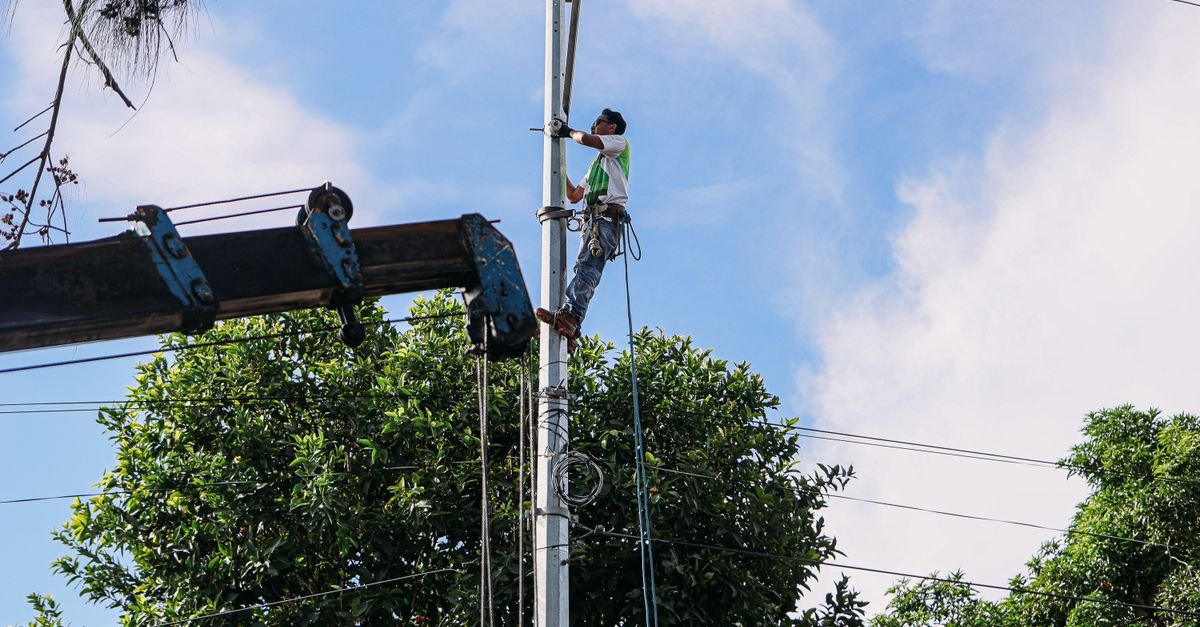 Eletricista sobe em poste de energia para fazer manutenção na rede sob céu azul