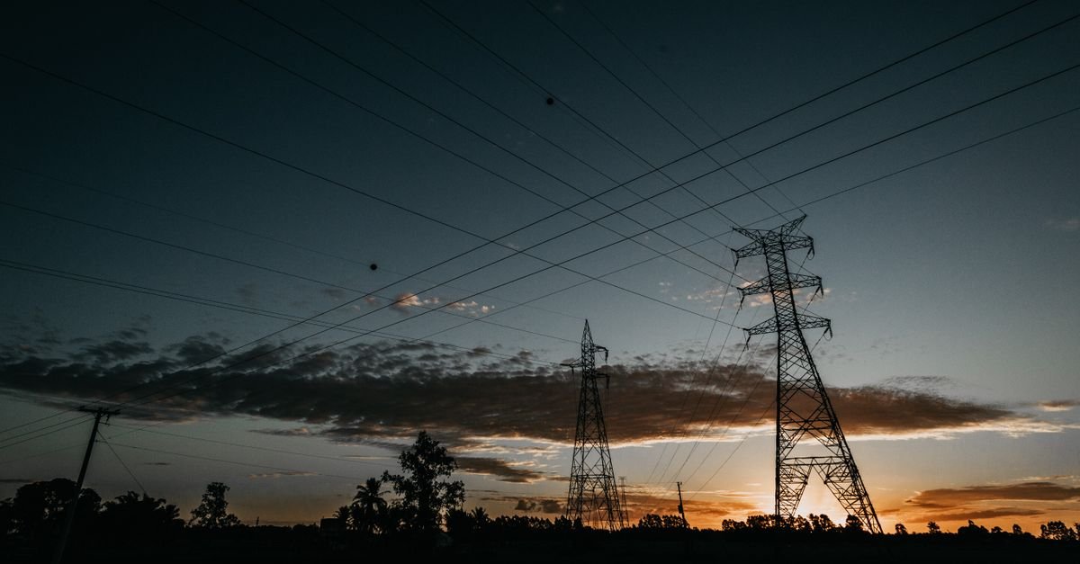 Torres de transmissão de energia elétrica em silhueta contra o céu no fim da tarde