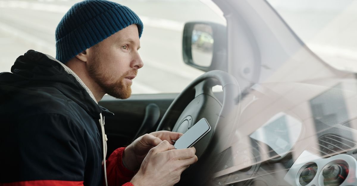 Homem dentro de um carro mexe no celular, ilustrando alerta sobre mensagens falsas em nome do Detran