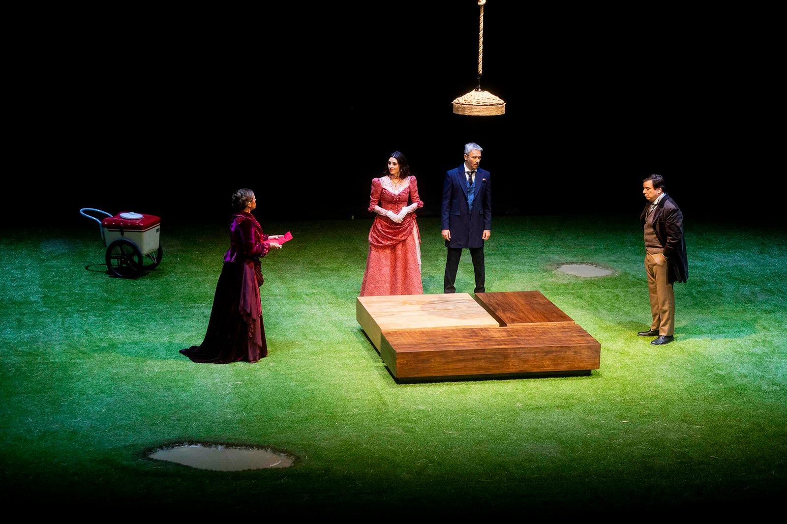 Quatro atores em cena de O Deus da Carnificina sobre palco coberto de grama