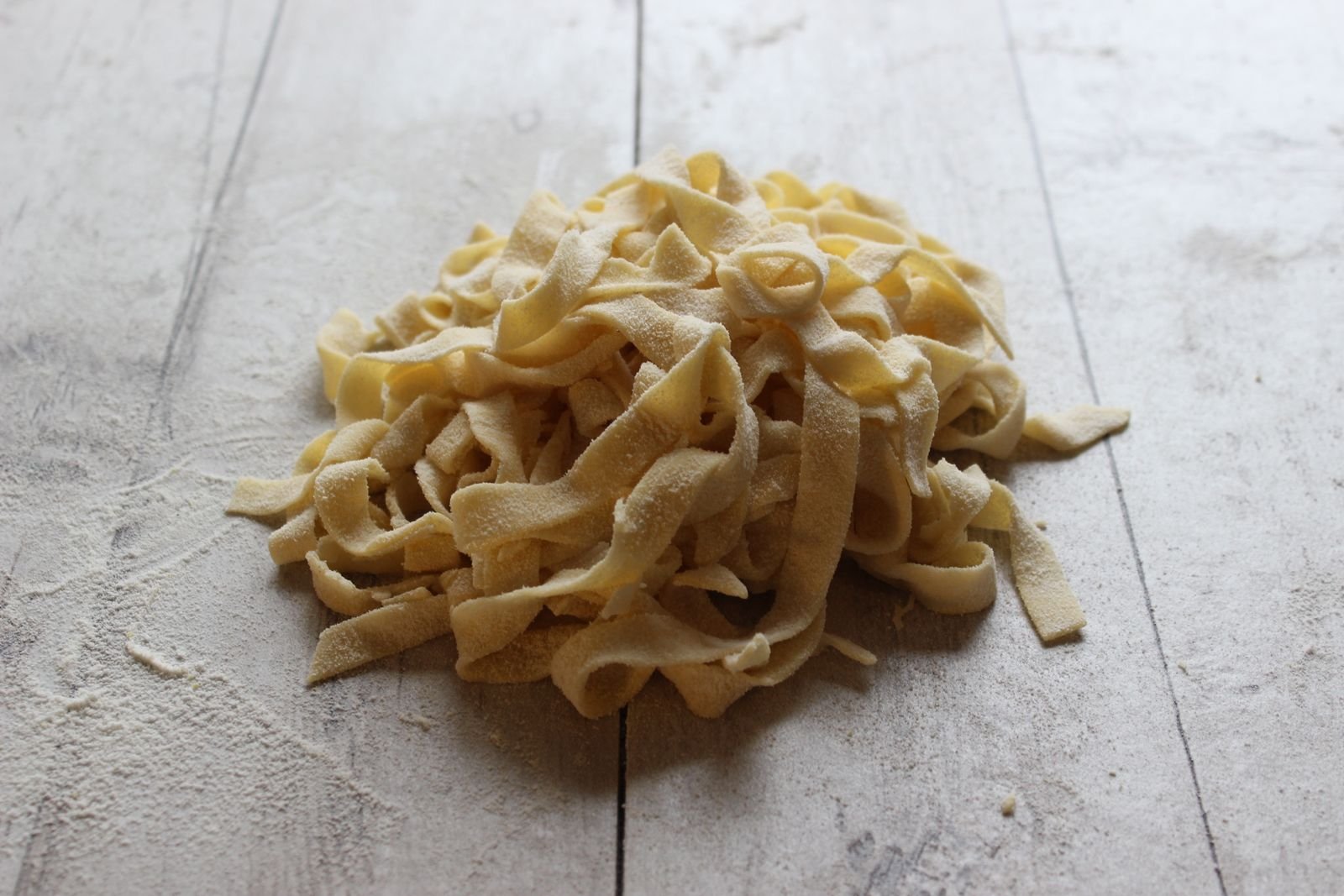 Massa fresca tipo tagliatelle sobre bancada de madeira com farinha