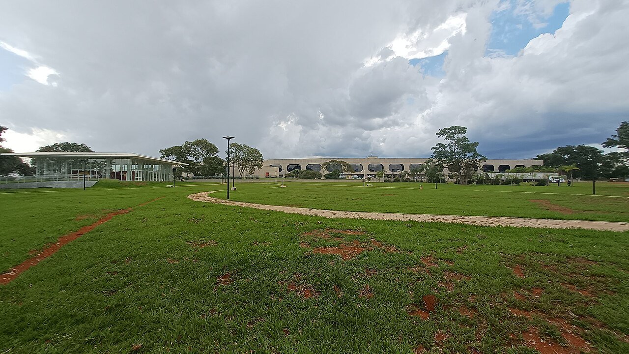 Gramado e caminho de pedra nos jardins do CCBB Brasília, com o pavilhão de vidro à esquerda e o prédio principal ao fundo