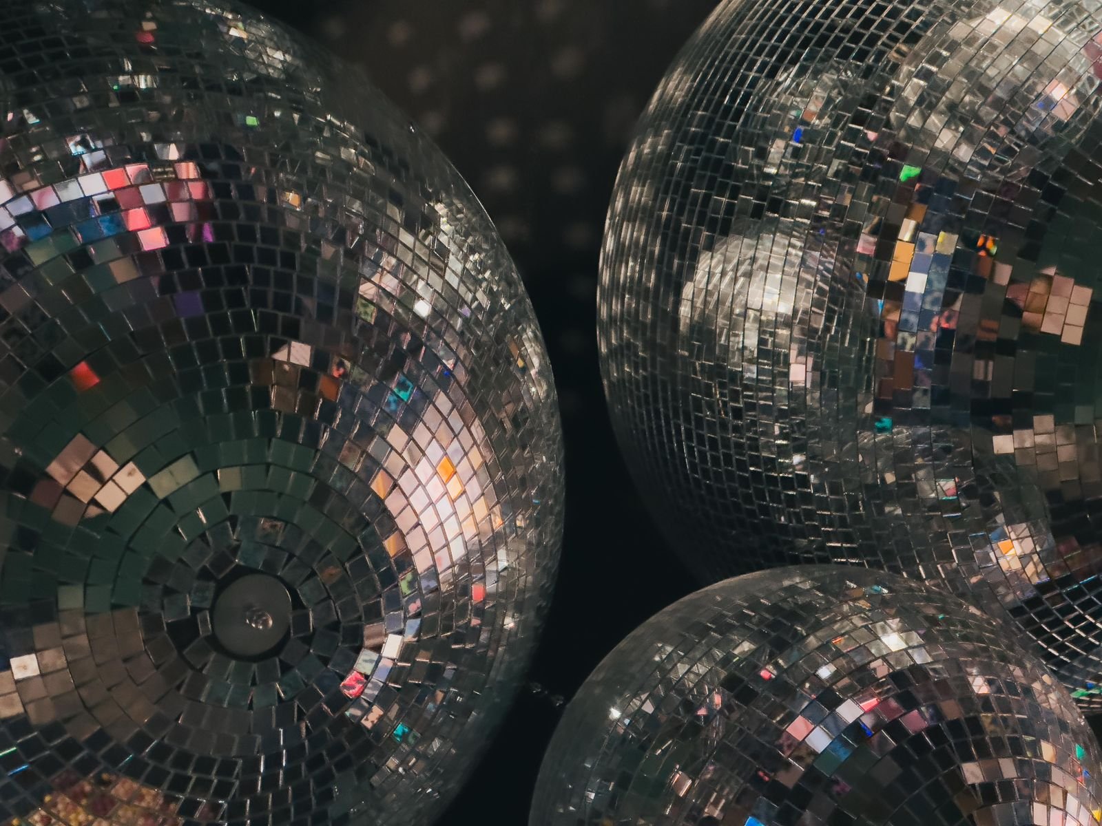 Três bolas de espelhos de discoteca vistas de perto, refletindo luzes coloridas
