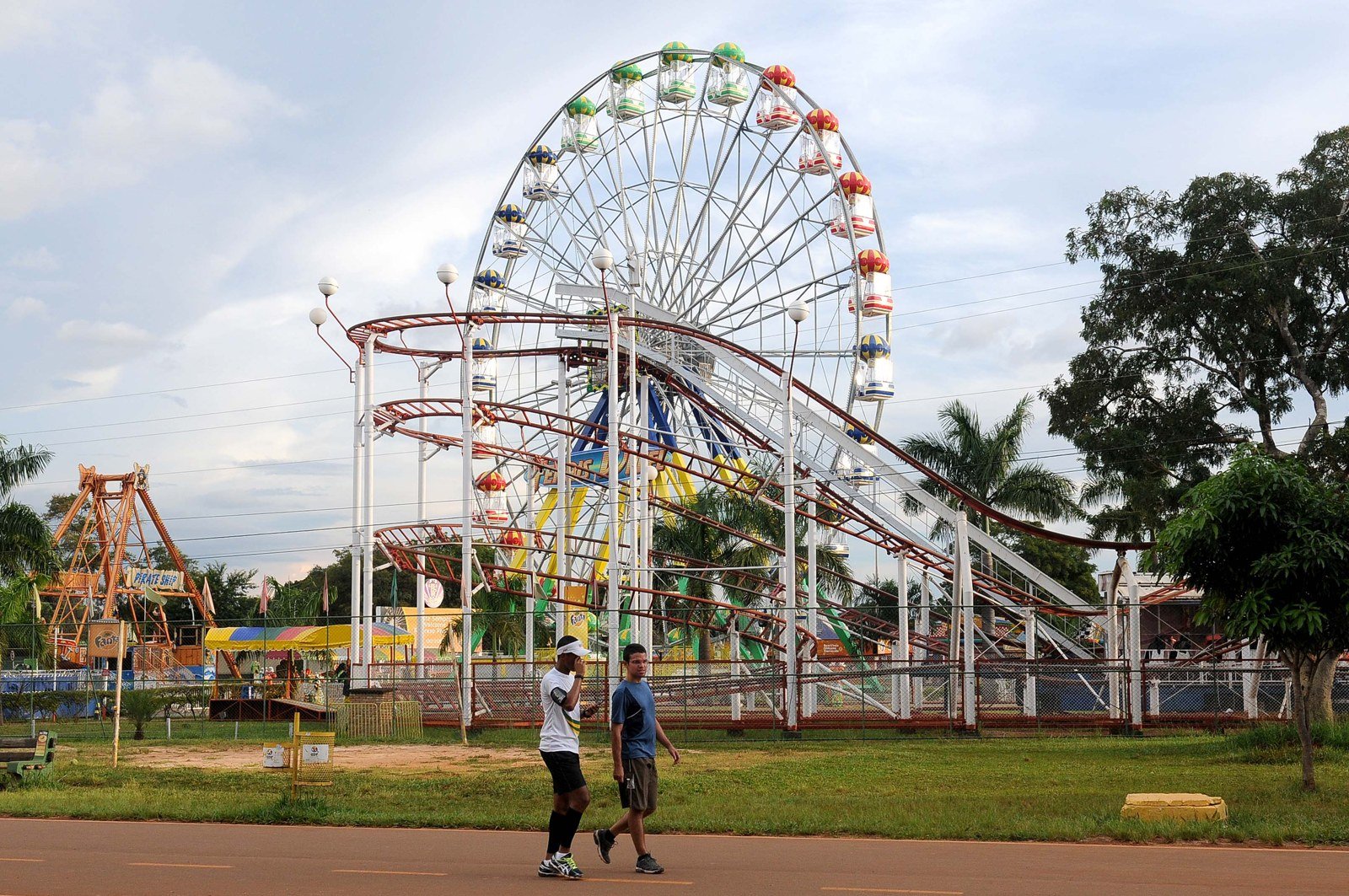 Duas pessoas caminham na pista do Parque da Cidade, em Brasília, diante da roda-gigante do parque de diversões