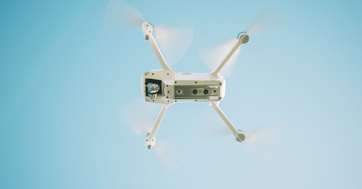 Drone branco em voo visto de baixo contra céu azul claro