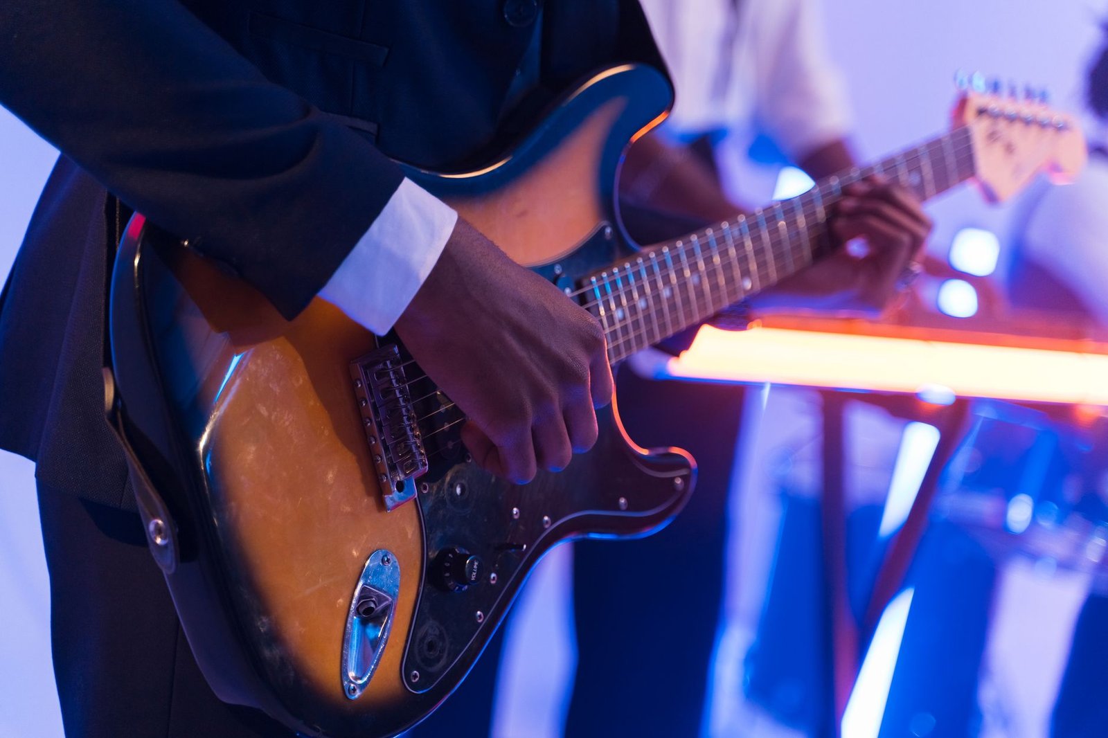 Guitarrista toca guitarra elétrica em palco com luzes azuis e laranja