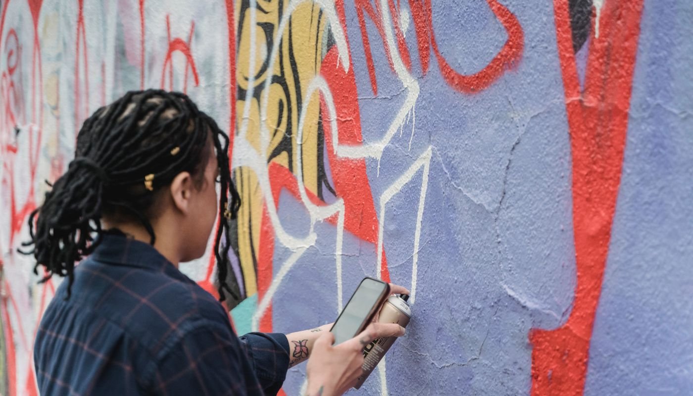 Artista pinta grafite colorido em um muro usando lata de spray